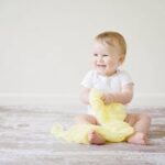 Adorable baby laughing while sitting on the floor with a yellow blanket indoors, showcasing happiness and innocence.